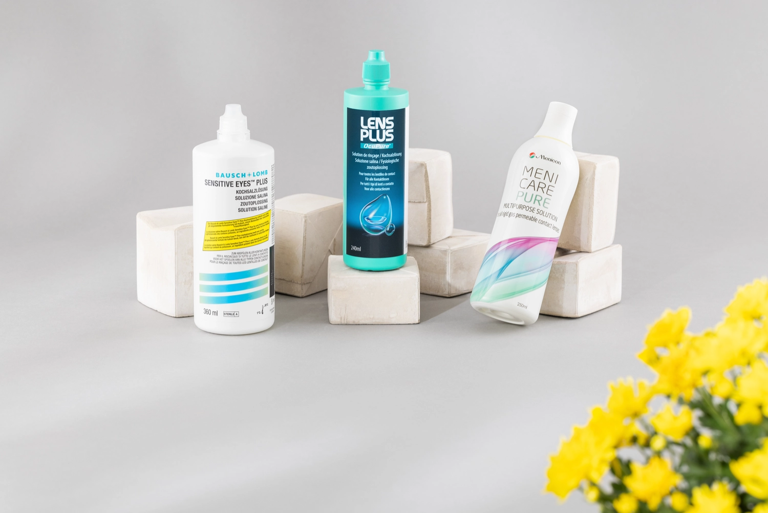 Drei Pflegeprodukte arrangiert mit einer gelben Blume im Vordergrund.